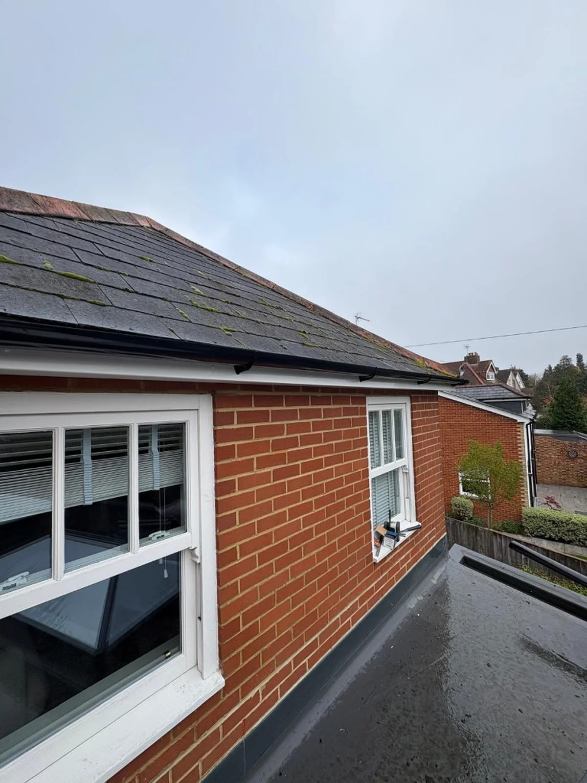 new white fascia and soffits with black guttering on a brick house with slate roof in Bagshot — Mitchell's Roofing